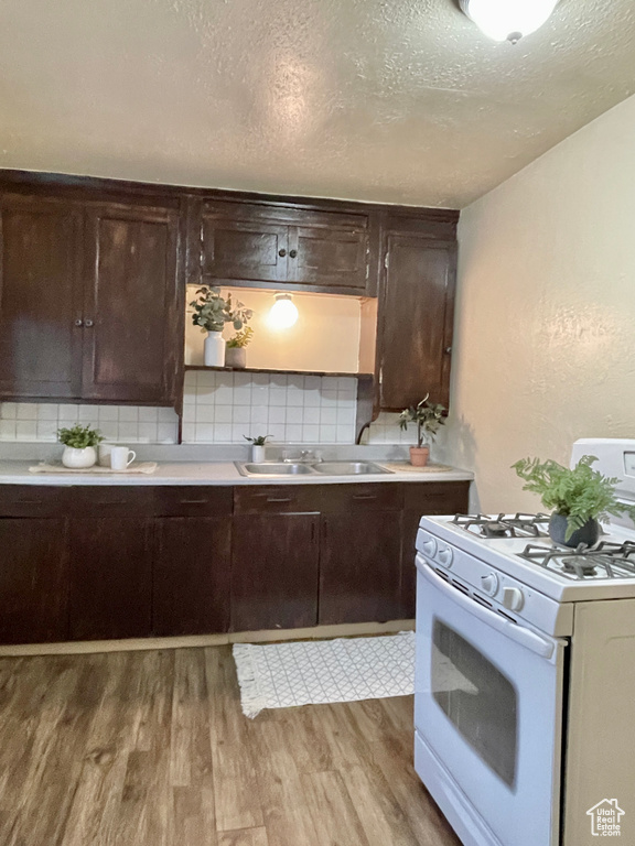 Kitchen featuring light wood-type flooring, decorative backsplash, white gas range oven, and sink