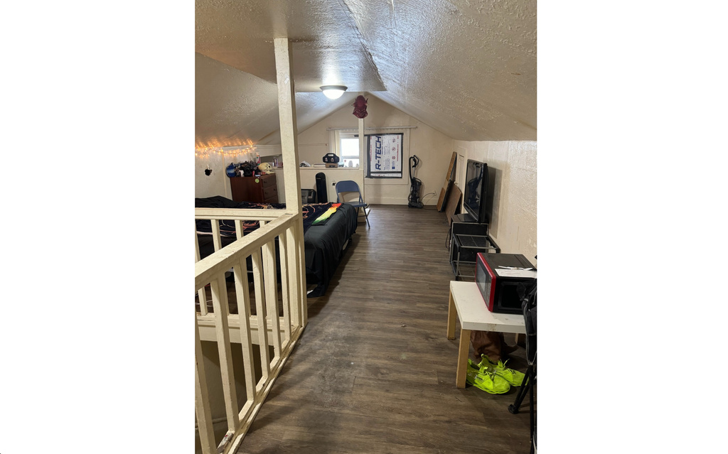 Hall featuring a textured ceiling, vaulted ceiling, and dark wood-type flooring