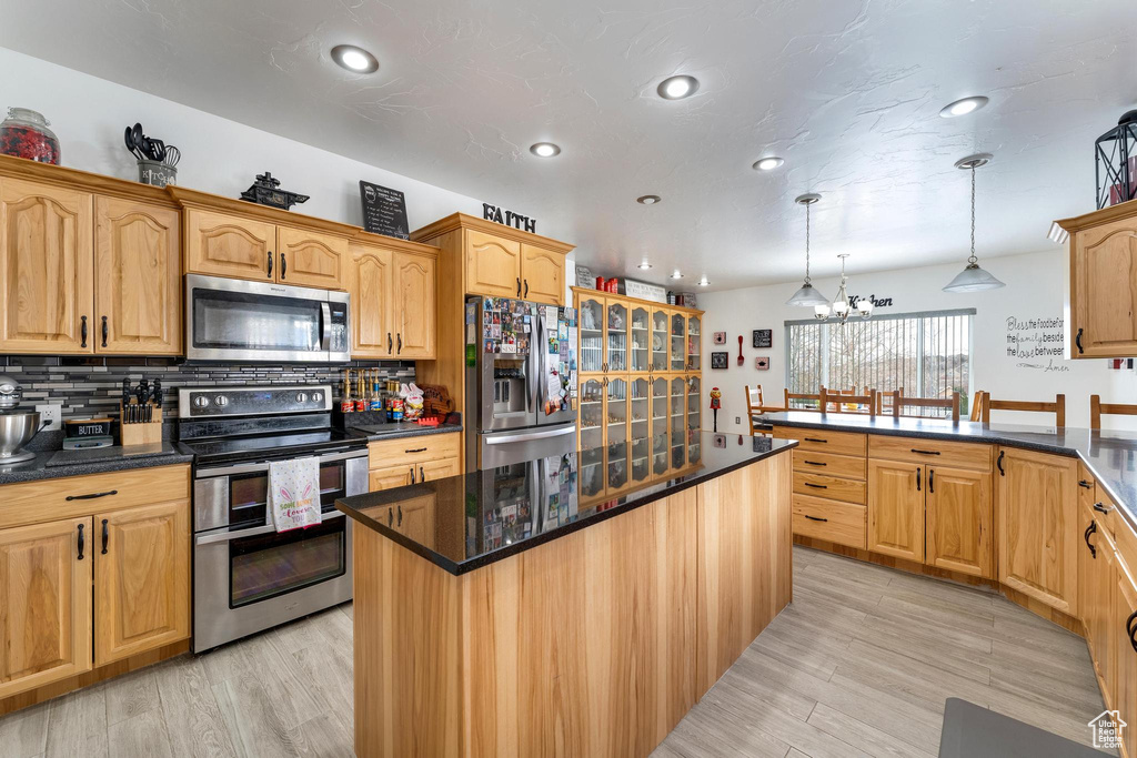 Kitchen with hanging light fixtures, an inviting chandelier, tasteful backsplash, light hardwood / wood-style flooring, and appliances with stainless steel finishes