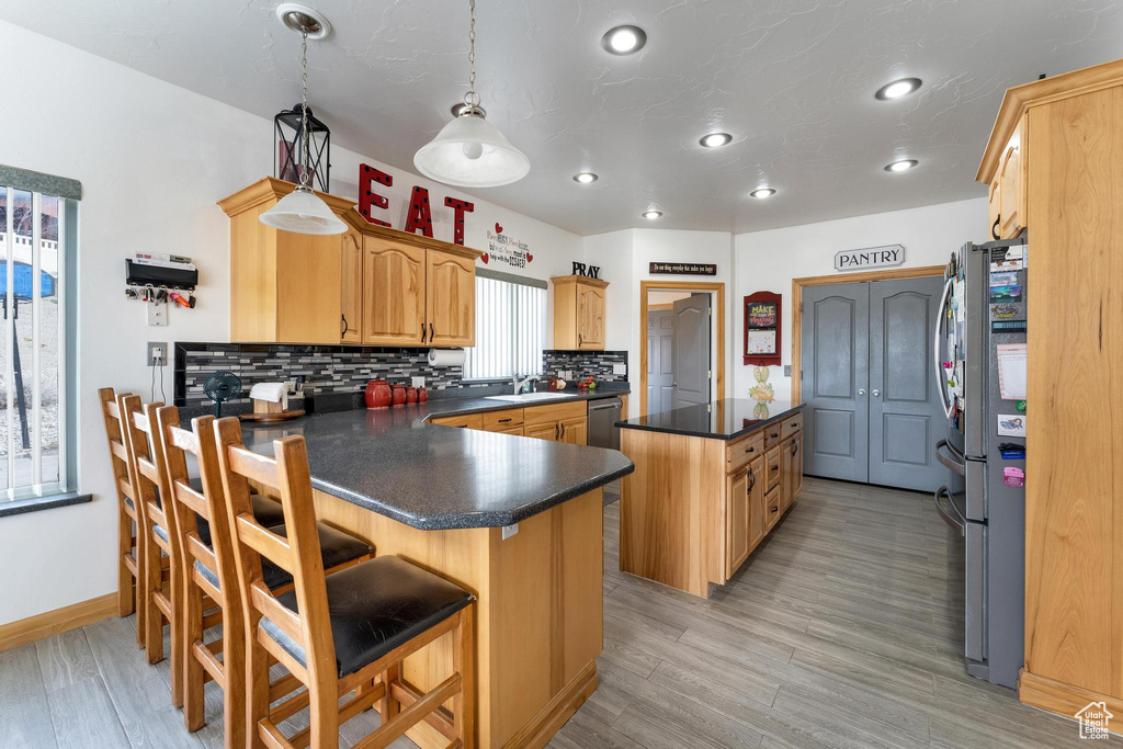 Kitchen featuring hanging light fixtures, a kitchen breakfast bar, tasteful backsplash, appliances with stainless steel finishes, and light wood-type flooring