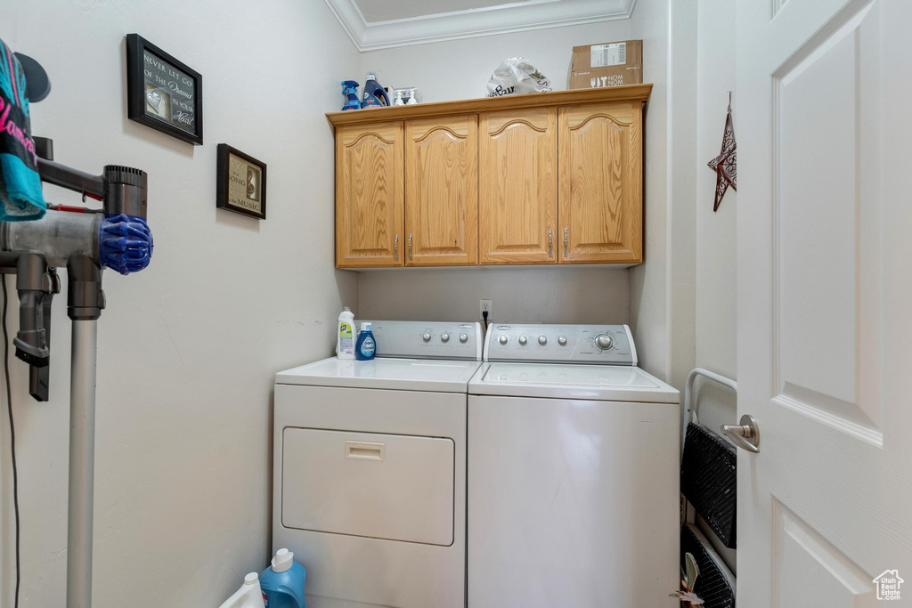 Clothes washing area featuring cabinets, washing machine and dryer, and ornamental molding