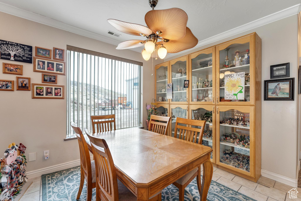 Tiled dining room with ceiling fan and crown molding
