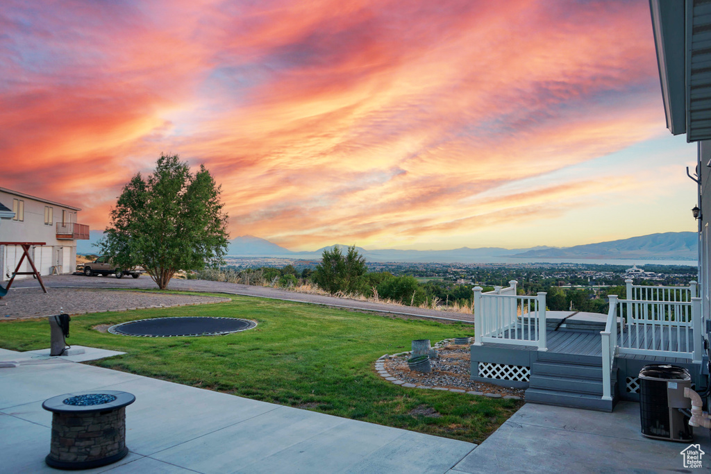 Yard at dusk with a deck with mountain view, a patio, and an outdoor fire pit