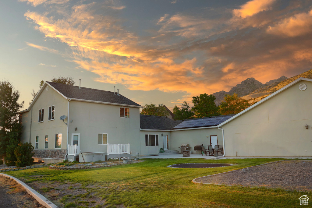 Back house at dusk with a lawn, a patio area, and a jacuzzi