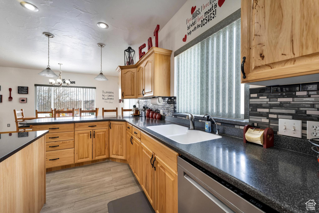 Kitchen with stainless steel dishwasher, sink, backsplash, and an inviting chandelier