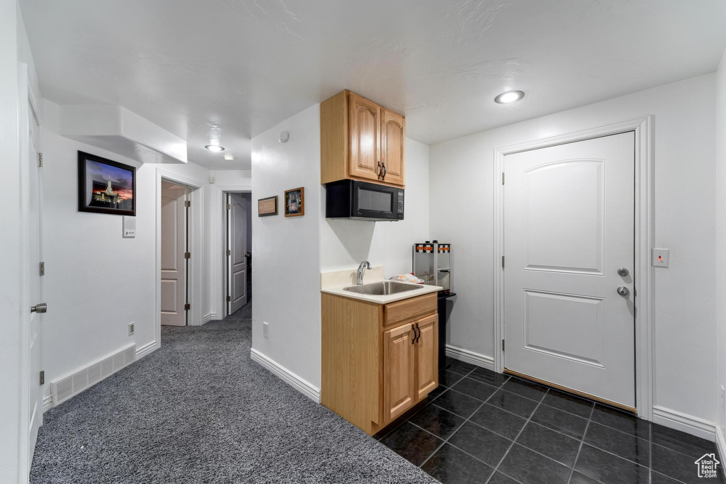 Kitchen with light brown cabinets, dark carpet, and sink
