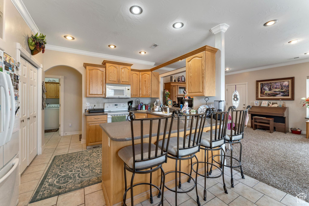 Kitchen featuring kitchen peninsula, washer / clothes dryer, crown molding, white appliances, and a kitchen bar