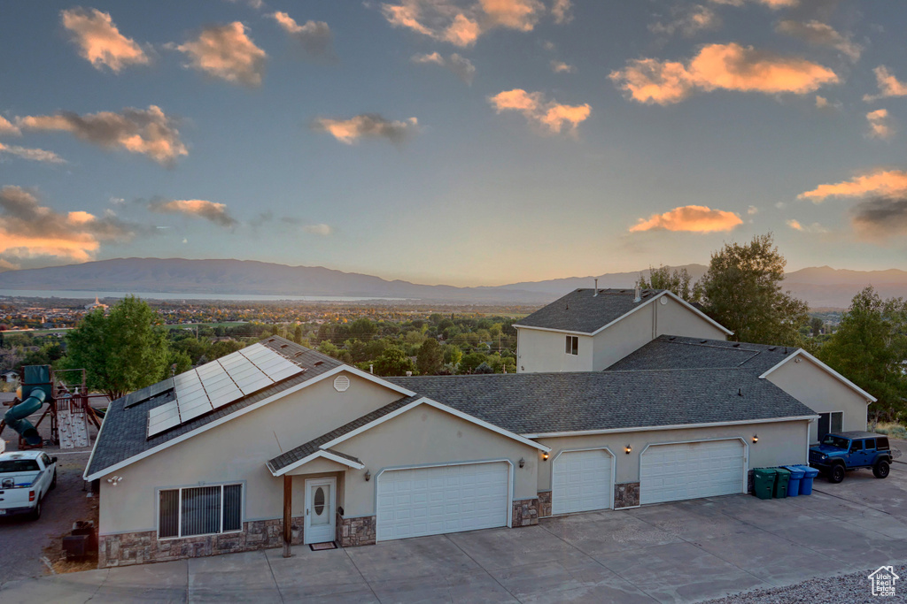 View of front of home with a mountain view, solar panels, a playground, and a garage
