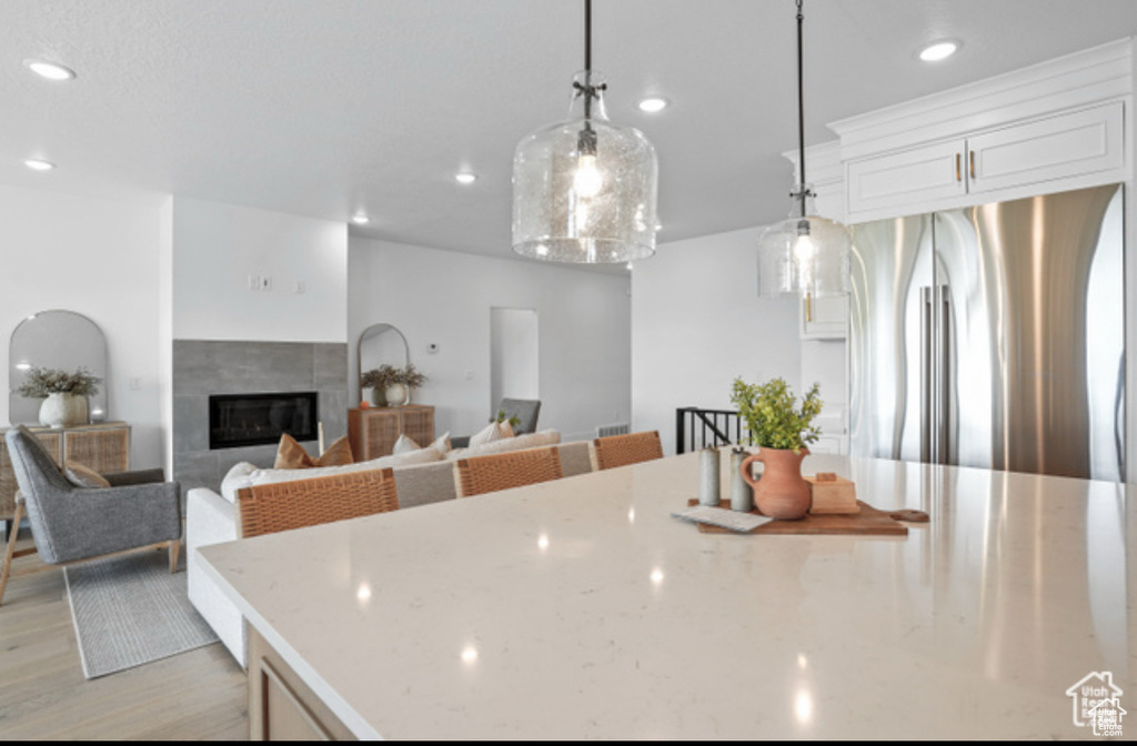 Kitchen with light hardwood / wood-style floors, stainless steel fridge, pendant lighting, a fireplace, and white cabinets