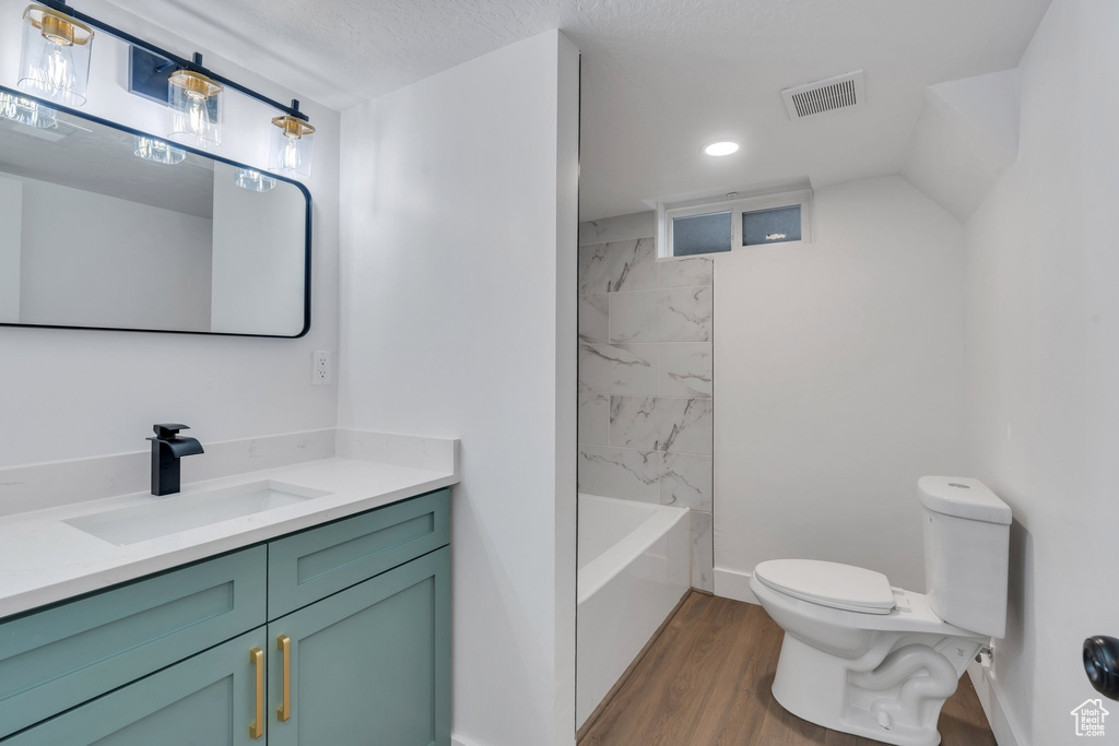 Full bathroom featuring a textured ceiling, toilet, hardwood / wood-style flooring, vanity, and tiled shower / bath