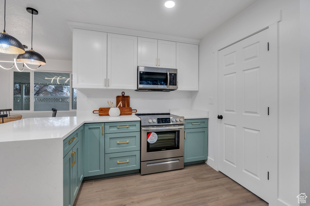 Kitchen with hanging light fixtures, kitchen peninsula, light hardwood / wood-style floors, white cabinets, and appliances with stainless steel finishes