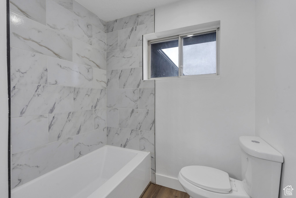 Bathroom with toilet, tiled shower / bath combo, and hardwood / wood-style flooring