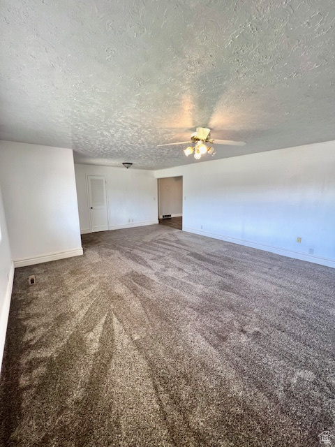 Unfurnished living room featuring a textured ceiling, a ceiling fan, carpet flooring, and baseboards