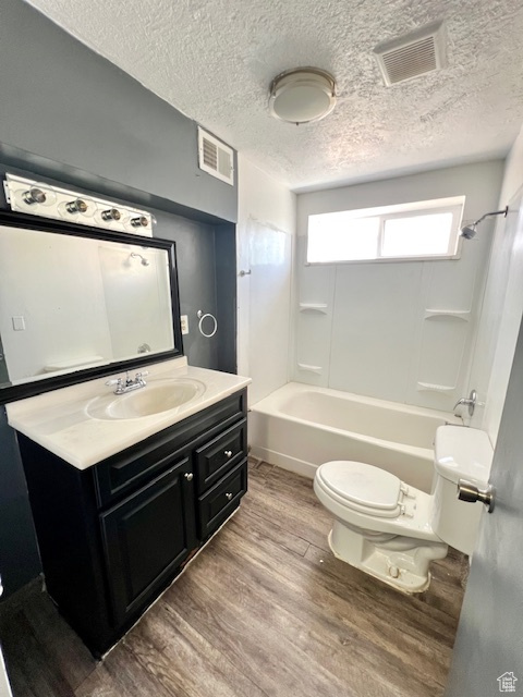 Full bathroom featuring wood finished floors, toilet, vanity, a textured ceiling, and bathing tub / shower combination