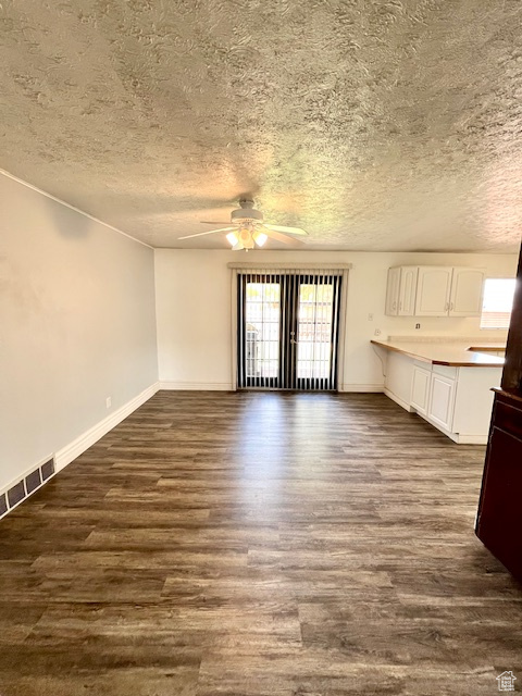 Unfurnished living room featuring a ceiling fan, a textured ceiling, dark wood finished floors, and baseboards