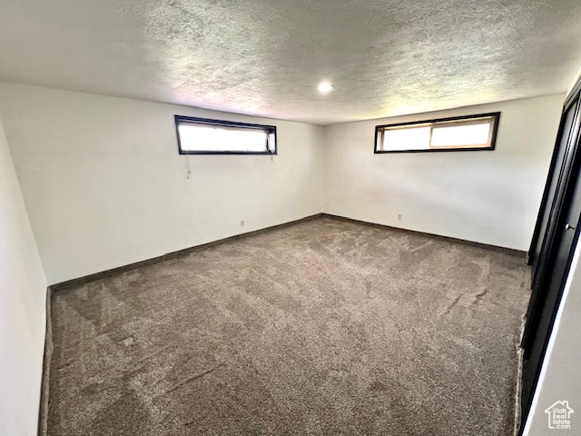 Carpeted empty room with a textured ceiling and baseboards