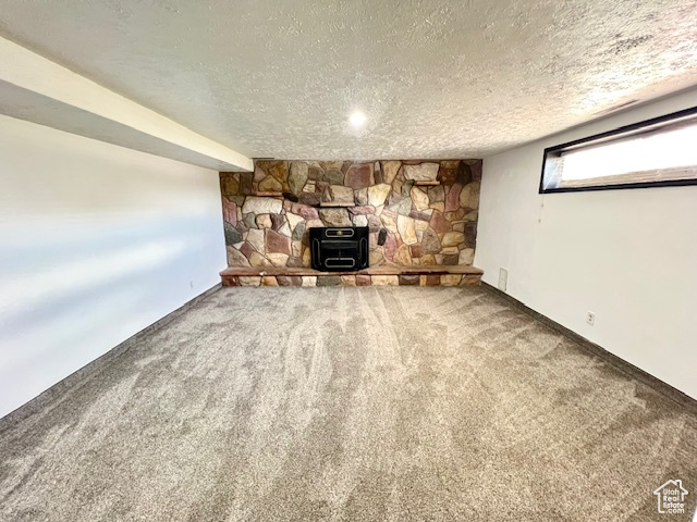 Unfurnished living room with a textured ceiling, a wood stove, carpet, and baseboards