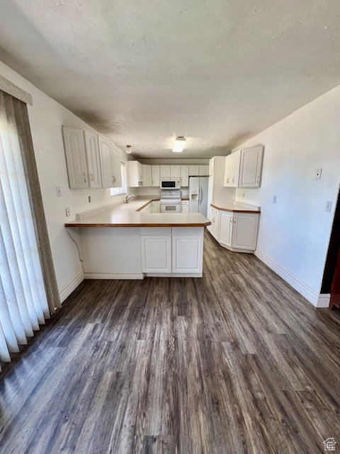 Kitchen featuring white appliances, a peninsula, dark wood-style flooring, baseboards, and a sink