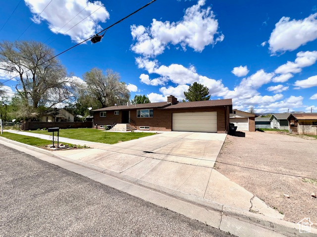 Single story home with an attached garage, concrete driveway, a front yard, and a chimney