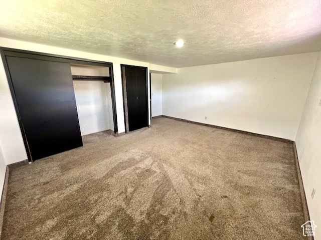 Unfurnished bedroom with multiple closets, a textured ceiling, carpet floors, and baseboards