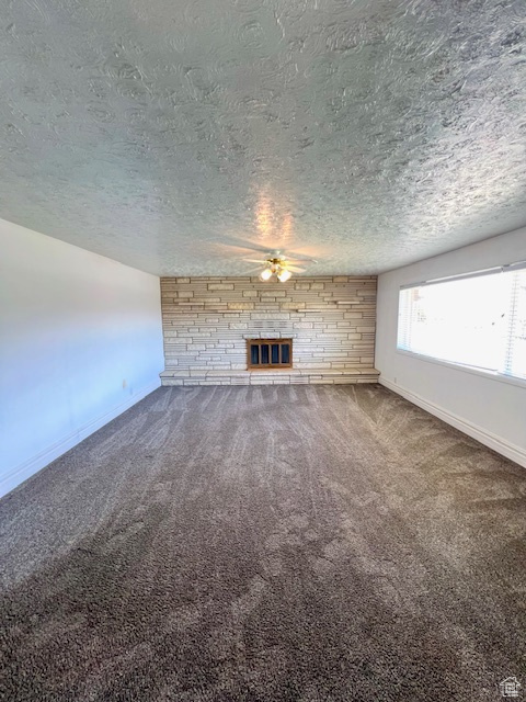 Unfurnished living room with a textured ceiling, a large fireplace, ceiling fan, carpet floors, and baseboards