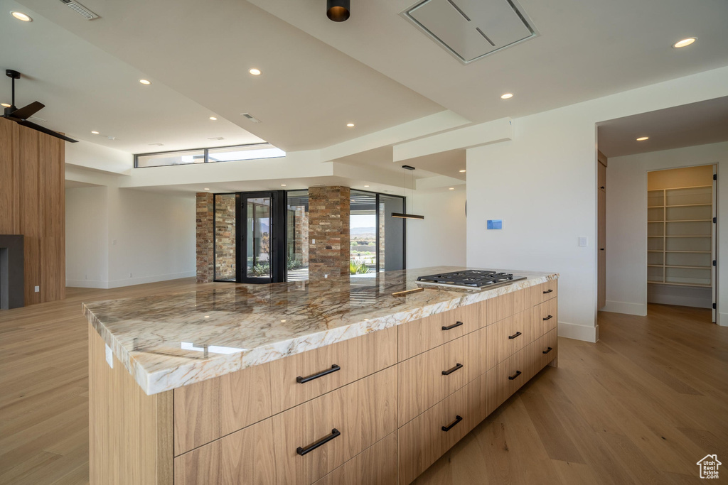 Kitchen featuring light stone countertops, light brown cabinetry, light wood-type flooring, stainless steel gas cooktop, and a large island