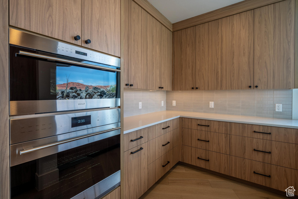 Kitchen with decorative backsplash, stainless steel double oven, and light brown cabinetry