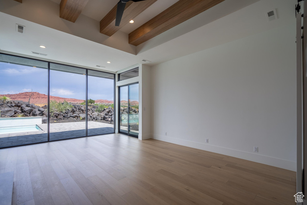 Unfurnished room with ceiling fan, beam ceiling, a barn door, a wall of windows, and a mountain view