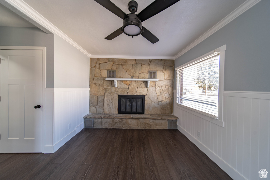 Unfurnished living room featuring dark wood-type flooring, a stone fireplace, ceiling fan, and ornamental molding
