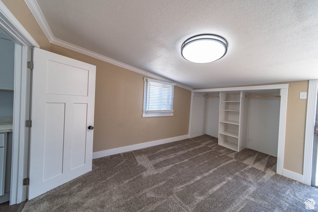 Unfurnished bedroom with dark colored carpet, a textured ceiling, a closet, and ornamental molding