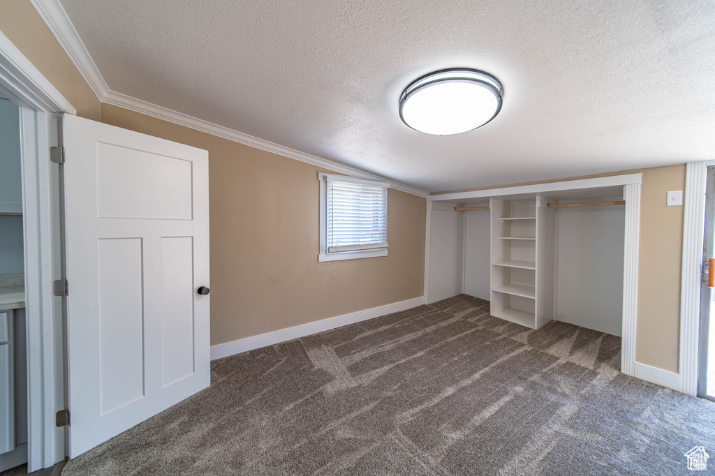 Unfurnished bedroom featuring dark carpet, crown molding, a textured ceiling, and a closet