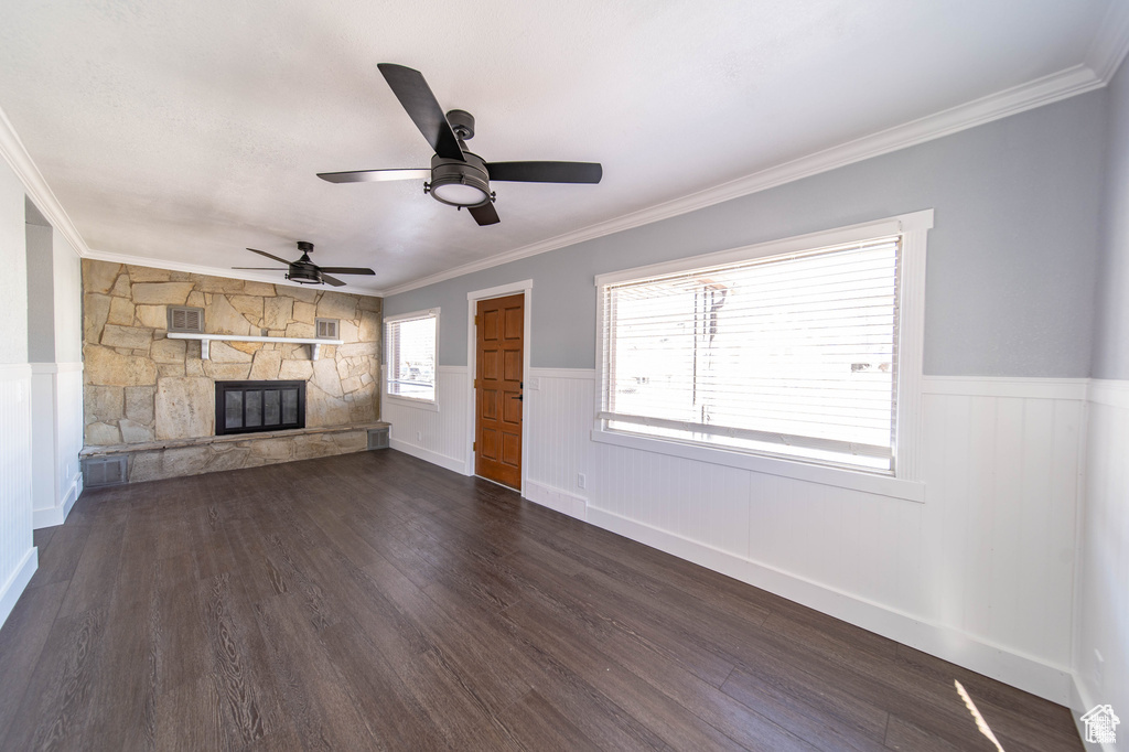 Unfurnished living room featuring dark hardwood / wood-style floors, a stone fireplace, ceiling fan, and crown molding