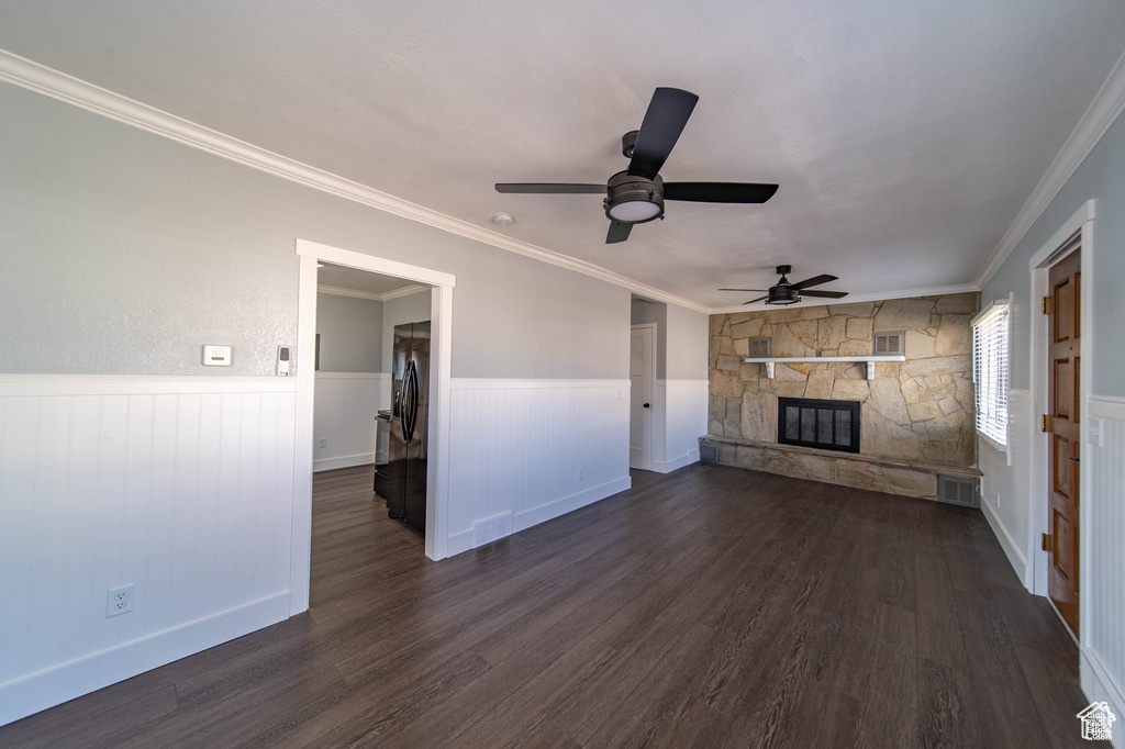 Unfurnished living room featuring ceiling fan, a fireplace, crown molding, and dark wood-type flooring