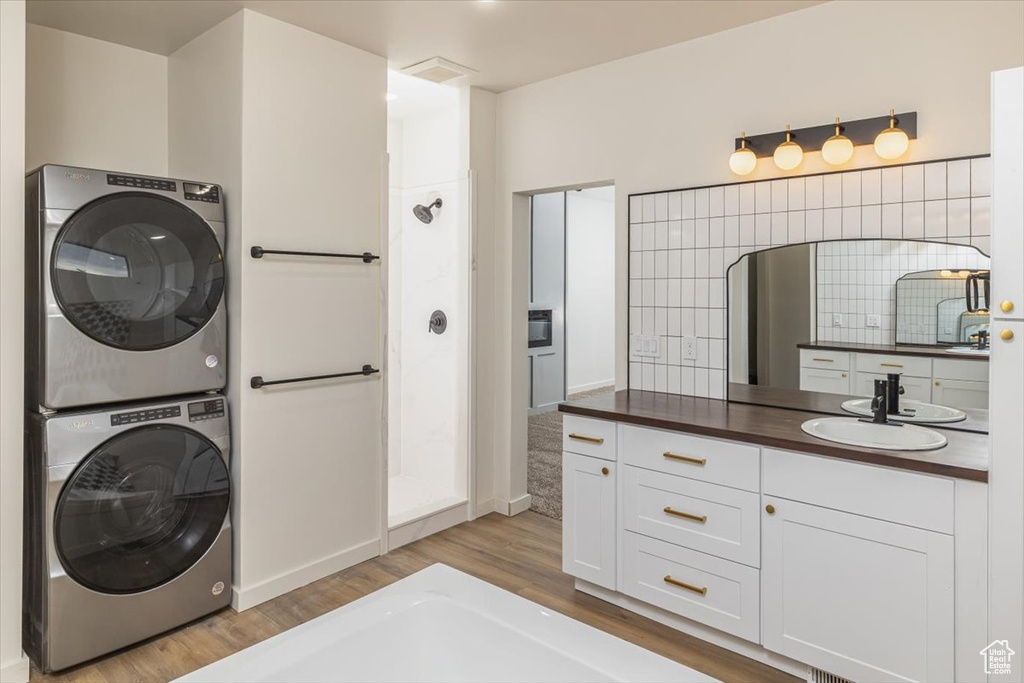 Washroom with sink, stacked washing maching and dryer, and light hardwood / wood-style flooring
