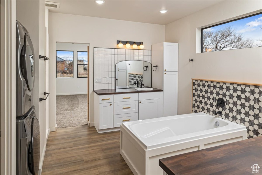 Bathroom with wood-type flooring, vanity, stacked washer and dryer, and a tub to relax in