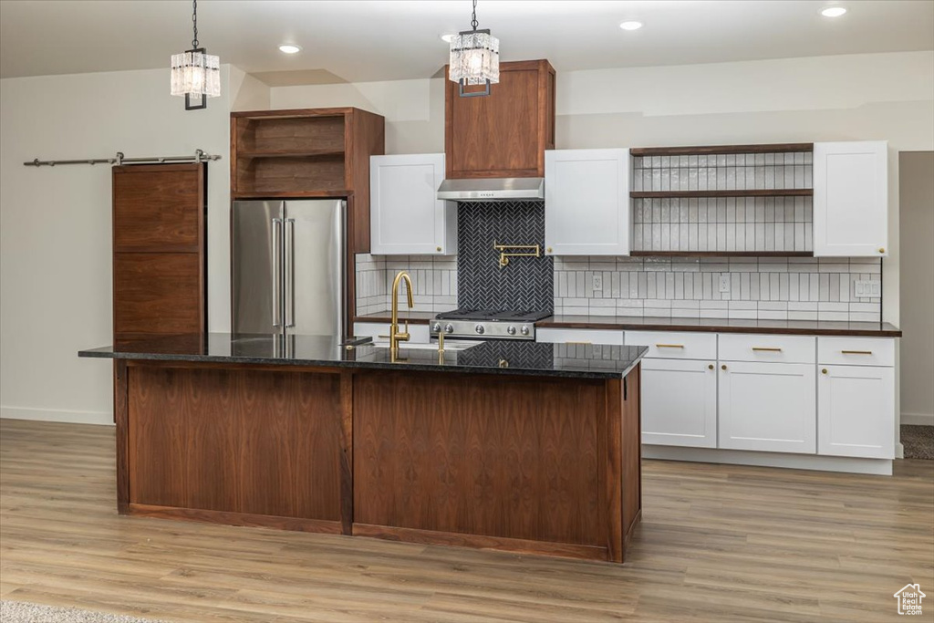 Kitchen with pendant lighting, premium appliances, white cabinetry, and a kitchen island with sink