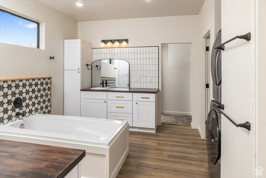 Bathroom featuring hardwood / wood-style floors, vanity, a tub, and stacked washer and clothes dryer
