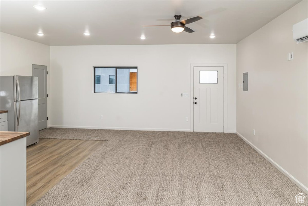 Unfurnished living room featuring light carpet, a wall unit AC, and ceiling fan