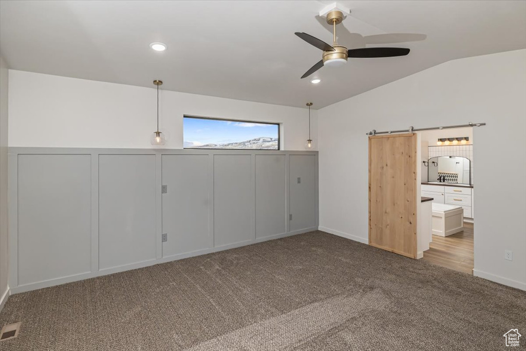 Unfurnished bedroom featuring a barn door, light colored carpet, vaulted ceiling, and ceiling fan