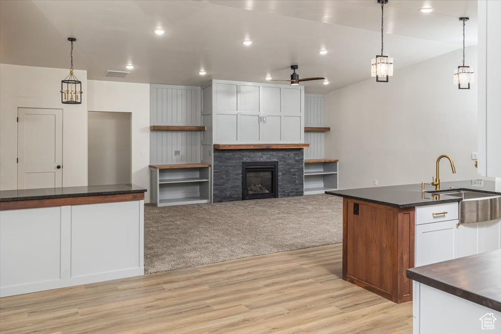 Kitchen with ceiling fan, sink, pendant lighting, a fireplace, and white cabinets