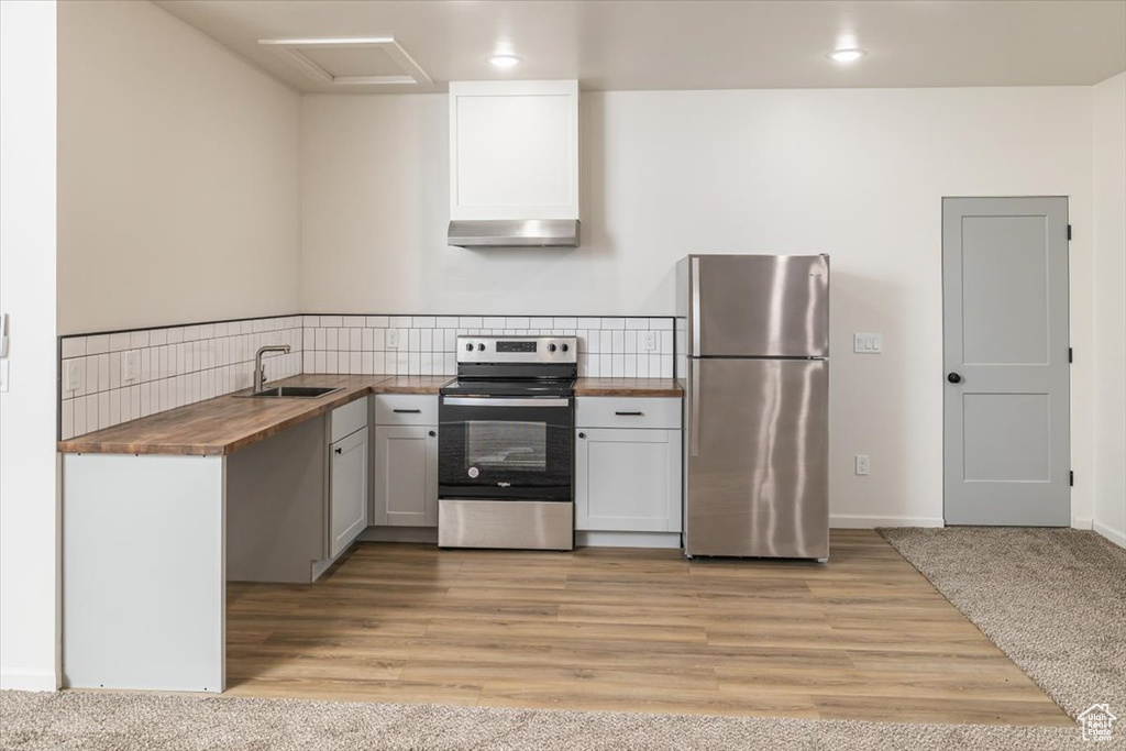 Kitchen featuring wooden counters, appliances with stainless steel finishes, light wood-type flooring, sink, and range hood