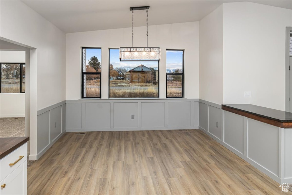 Unfurnished dining area featuring an inviting chandelier, lofted ceiling, and light wood-type flooring