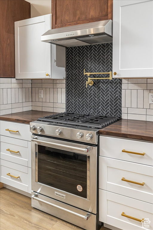 Kitchen featuring tasteful backsplash, stainless steel range, white cabinets, and ventilation hood
