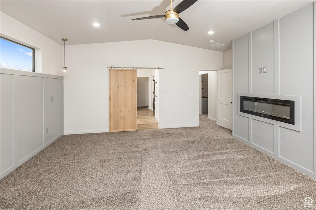 Unfurnished living room featuring a barn door, ceiling fan, light colored carpet, and lofted ceiling