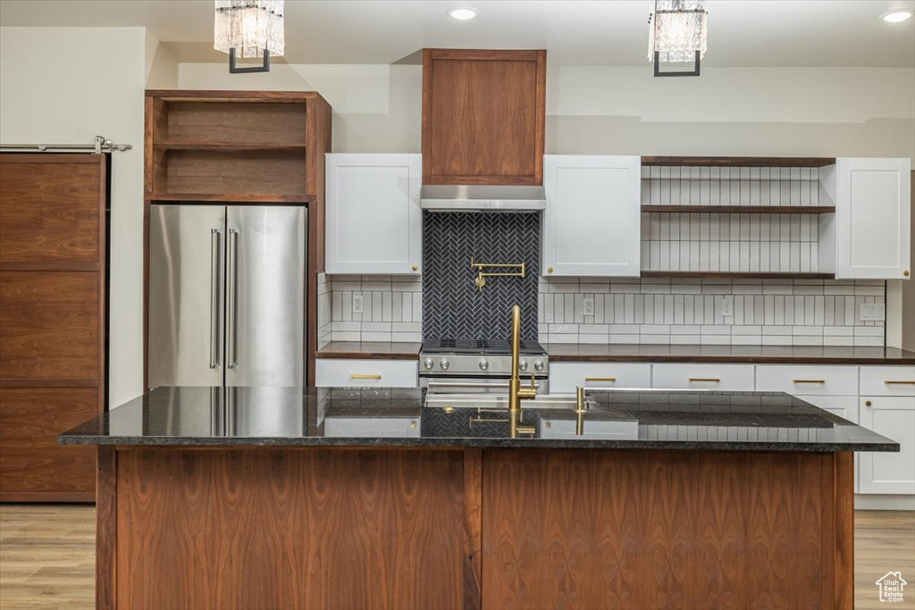 Kitchen featuring white cabinetry, a center island, premium appliances, tasteful backsplash, and light hardwood / wood-style flooring