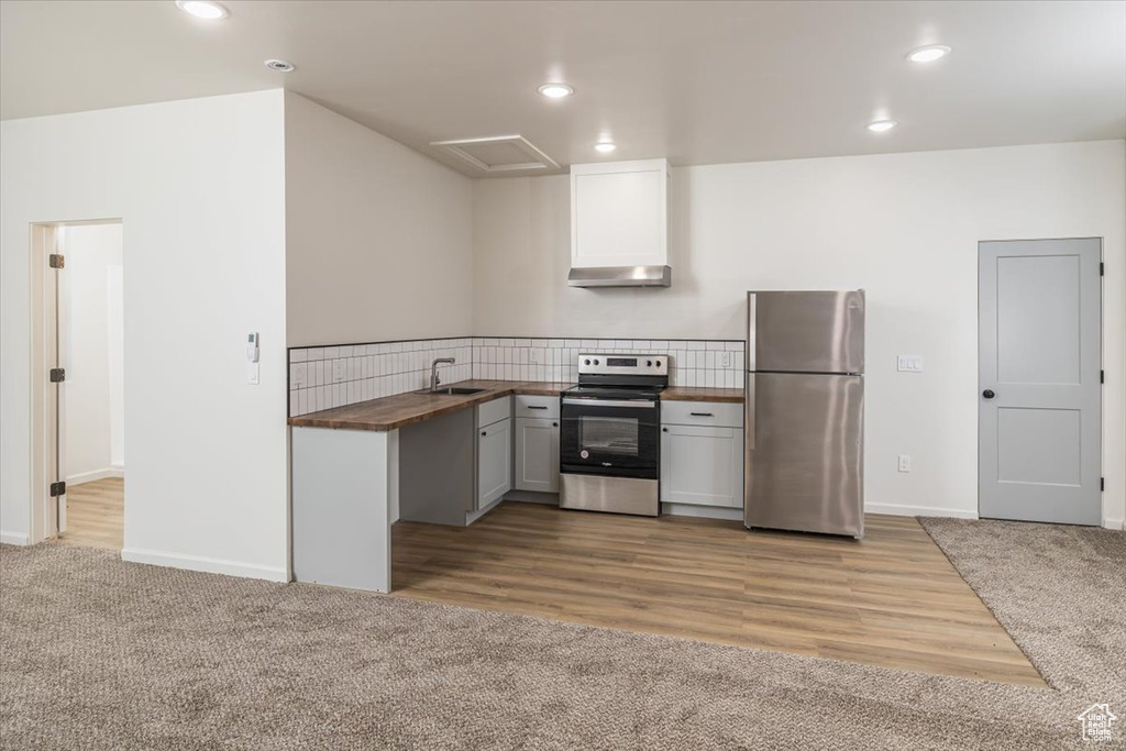 Kitchen featuring light carpet, sink, wall chimney exhaust hood, appliances with stainless steel finishes, and butcher block countertops