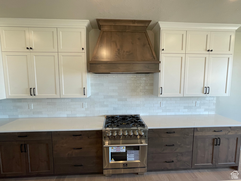 Kitchen featuring high end stainless steel range oven, decorative backsplash, white cabinetry, and premium range hood