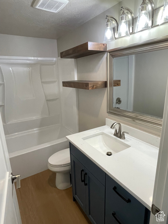 Full bathroom with vanity, a textured ceiling, shower / bathing tub combination, hardwood / wood-style flooring, and toilet