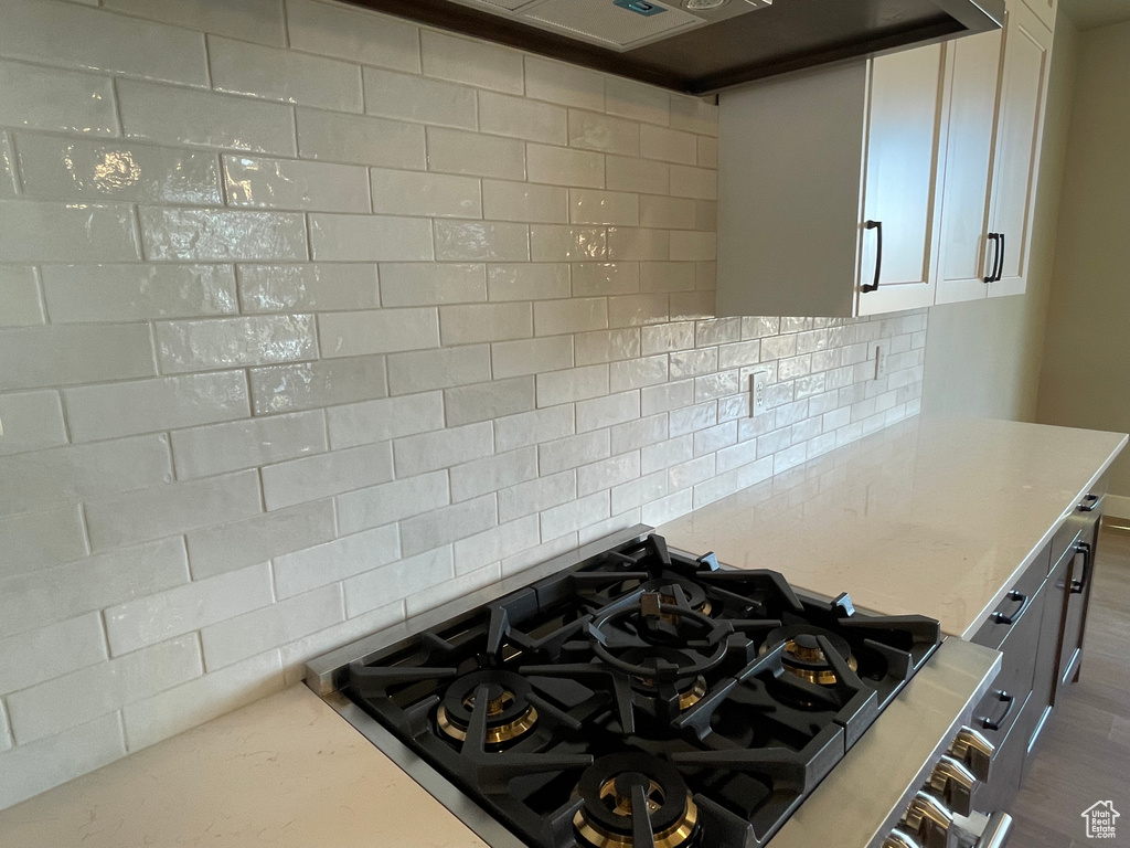 Kitchen featuring cooktop, light stone counters, backsplash, and dark wood-type flooring