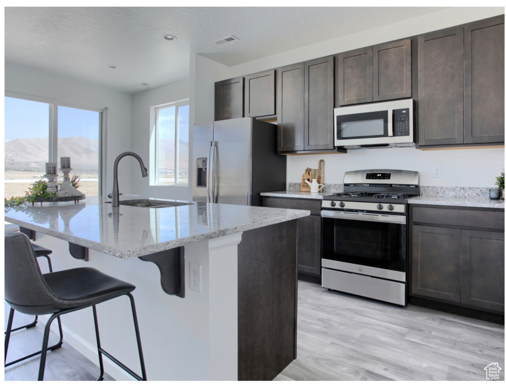 Kitchen featuring light stone countertops, sink, stainless steel appliances, a mountain view, and a breakfast bar area